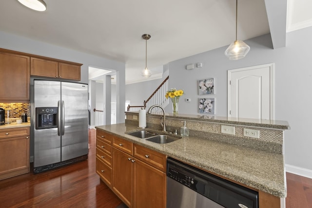 kitchen with stainless steel appliances, brown cabinetry, a sink, and light stone countertops