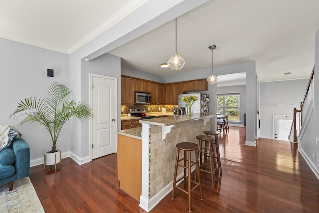 kitchen with brown cabinetry, decorative backsplash, light stone counters, appliances with stainless steel finishes, and hanging light fixtures