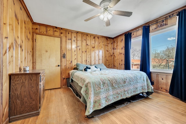 bedroom with light wood finished floors, wooden walls, a ceiling fan, and crown molding