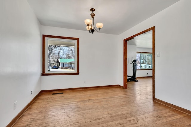 spare room featuring light wood-type flooring, visible vents, a notable chandelier, and baseboards