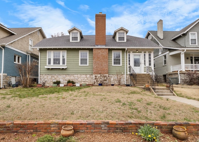 view of front of home with stone siding, a shingled roof, a chimney, and a front lawn