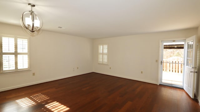 unfurnished room featuring dark wood-style flooring, an inviting chandelier, visible vents, and baseboards