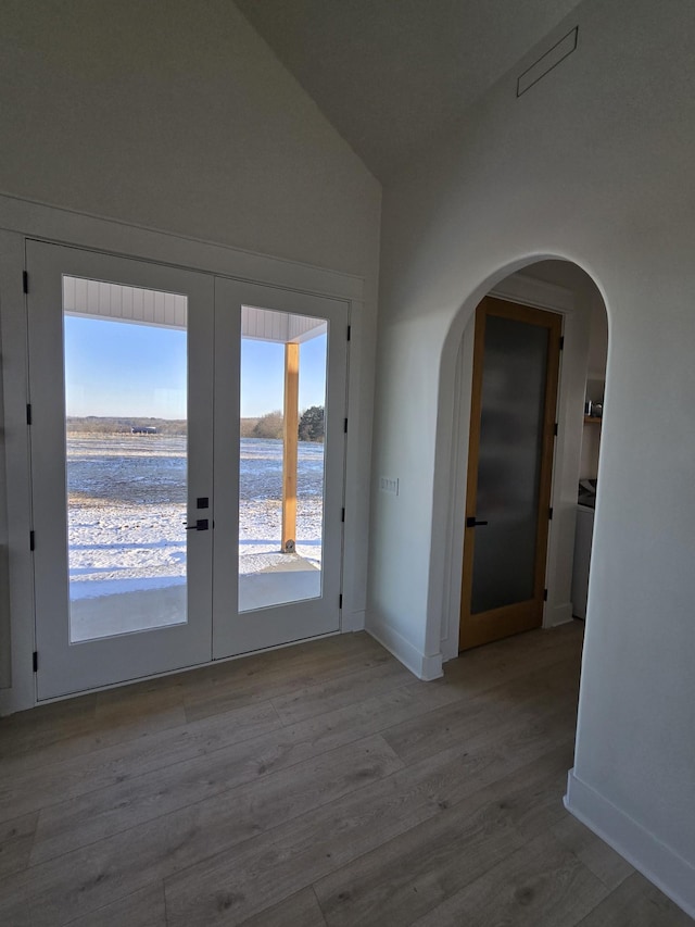 doorway with arched walkways, french doors, lofted ceiling, light wood-style floors, and baseboards