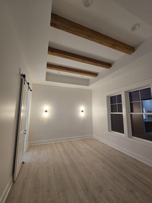 unfurnished room with light wood-style floors, a barn door, baseboards, and beamed ceiling