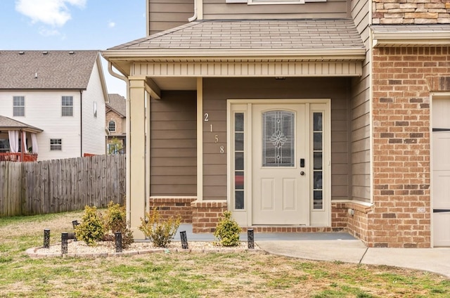 property entrance featuring brick siding, roof with shingles, and fence