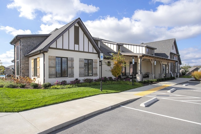 exterior space featuring uncovered parking, stone siding, a front lawn, and roof with shingles