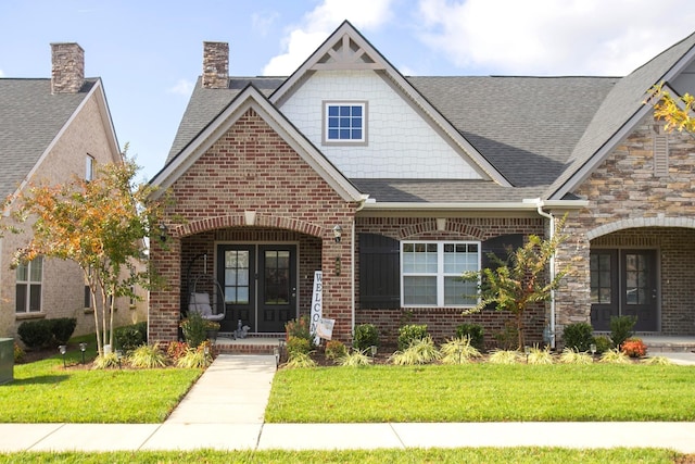 view of front of property with a porch, a front yard, brick siding, and roof with shingles