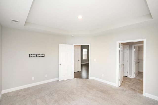 unfurnished bedroom with carpet floors, a tray ceiling, and visible vents