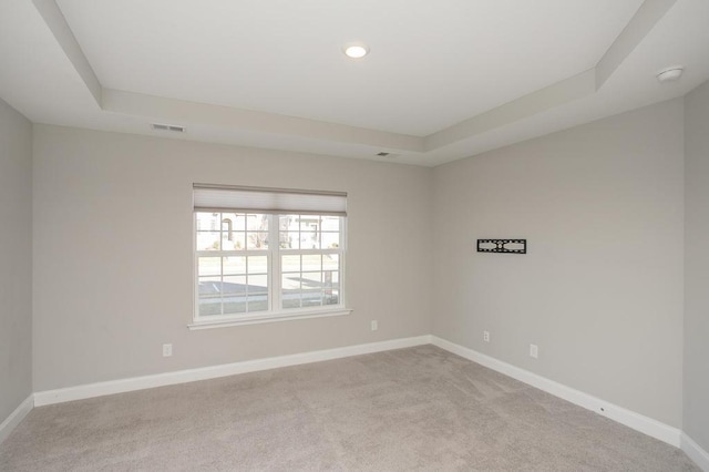 spare room featuring visible vents, a raised ceiling, light colored carpet, and baseboards