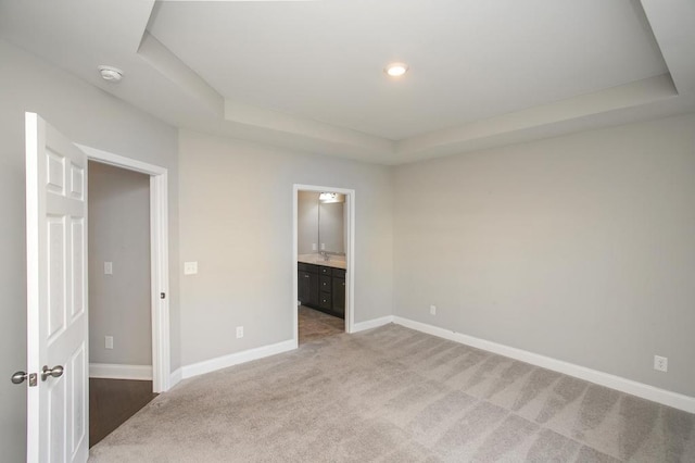 unfurnished bedroom with recessed lighting, a raised ceiling, light carpet, connected bathroom, and baseboards