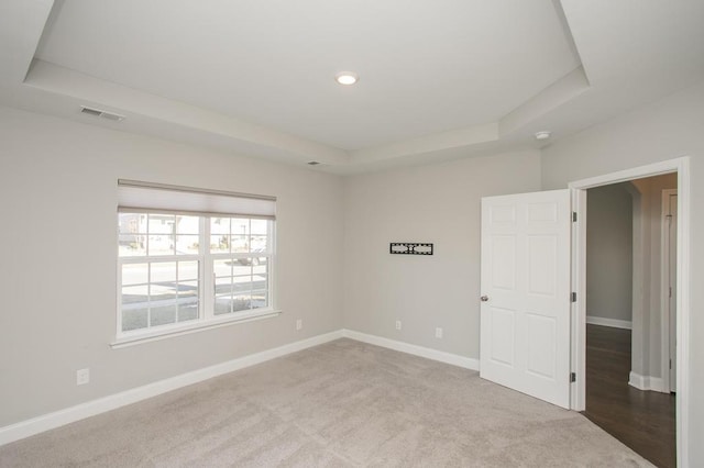 spare room with a raised ceiling, visible vents, and baseboards