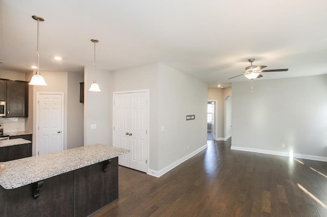 kitchen with a breakfast bar, pendant lighting, a center island, arched walkways, and dark brown cabinetry