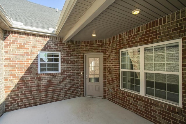 view of exterior entry featuring brick siding and a patio area