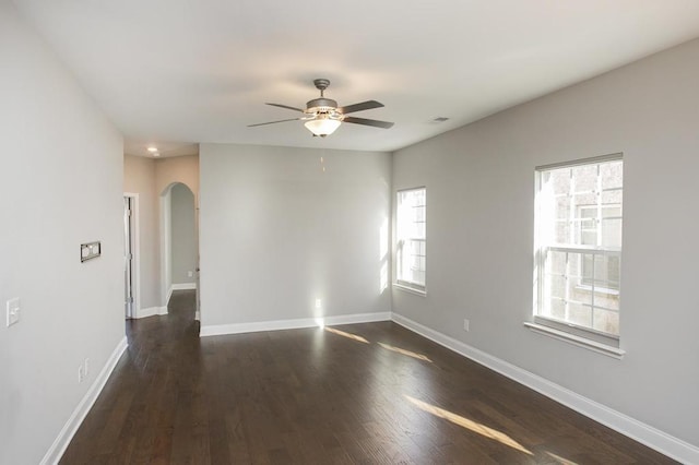 empty room featuring arched walkways, visible vents, a ceiling fan, baseboards, and dark wood finished floors