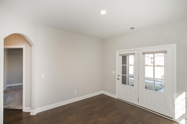 interior space with arched walkways, dark wood-style flooring, visible vents, and baseboards