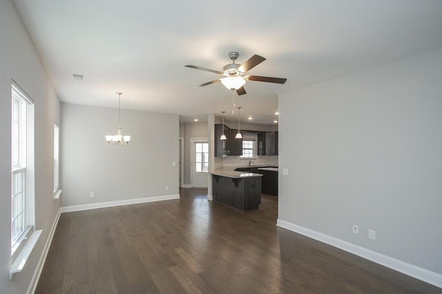 unfurnished living room featuring dark wood-type flooring, visible vents, baseboards, and ceiling fan with notable chandelier