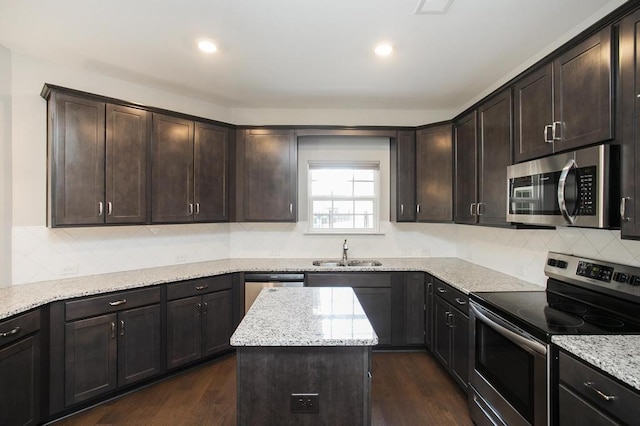 kitchen with stainless steel appliances, light stone counters, a sink, and a center island