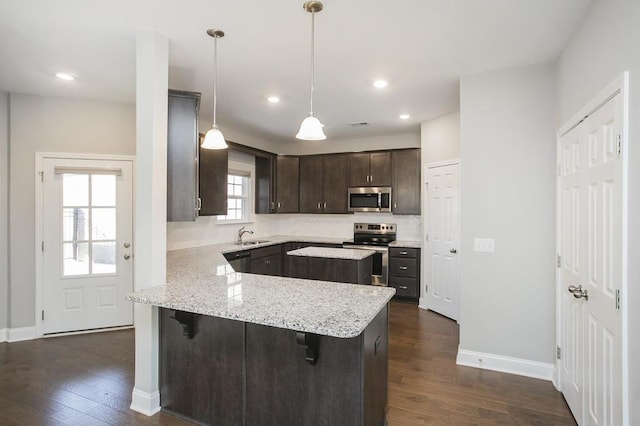 kitchen with pendant lighting, appliances with stainless steel finishes, dark wood-type flooring, a peninsula, and a kitchen breakfast bar