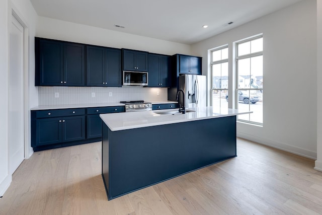 kitchen featuring a kitchen island with sink, a sink, light countertops, appliances with stainless steel finishes, and light wood finished floors