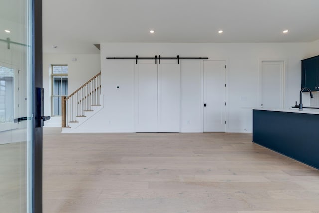 unfurnished living room featuring light wood-type flooring, a barn door, stairway, and a sink