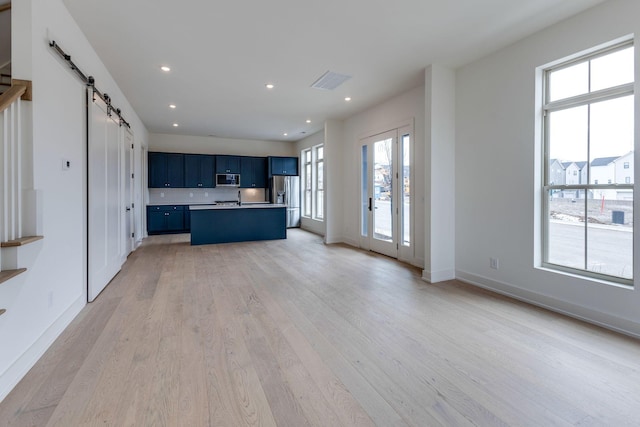 kitchen with a barn door, a breakfast bar area, blue cabinets, a kitchen island with sink, and light countertops