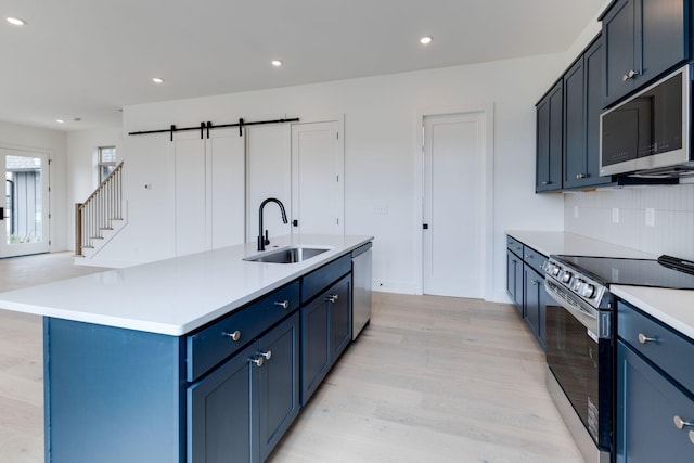 kitchen featuring a barn door, appliances with stainless steel finishes, a kitchen island with sink, light countertops, and a sink