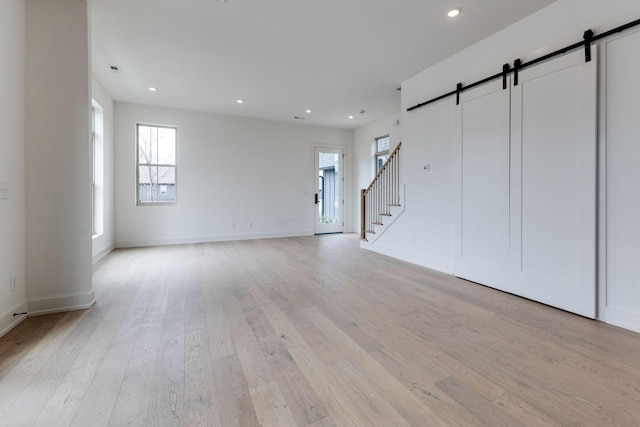 unfurnished living room featuring stairs, a barn door, light wood-type flooring, and recessed lighting