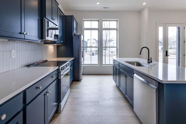 kitchen featuring stainless steel appliances, an island with sink, a sink, and blue cabinets