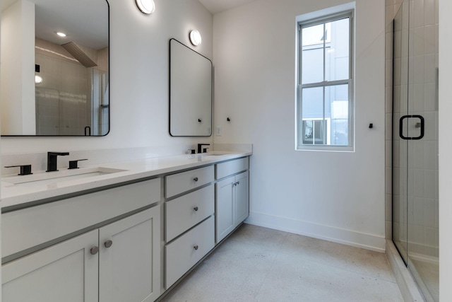 bathroom with double vanity, a stall shower, a sink, and baseboards