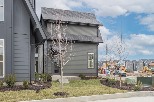 view of side of home with a yard, a shingled roof, and a residential view