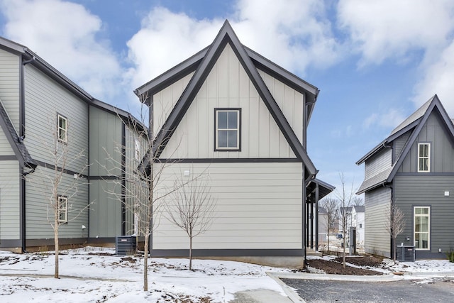 snow covered property with board and batten siding and central air condition unit