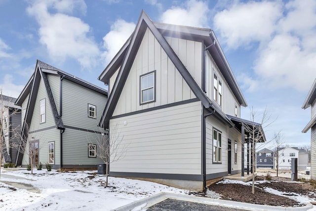 view of snow covered exterior with central AC and board and batten siding