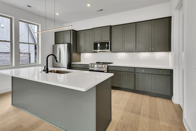 kitchen with a center island with sink, backsplash, stainless steel appliances, light countertops, and a sink