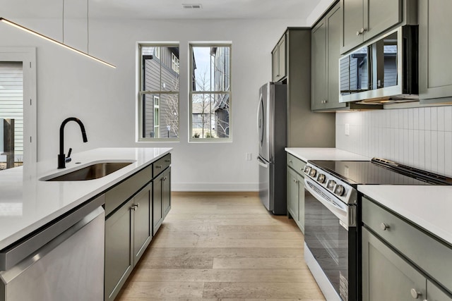 kitchen with stainless steel appliances, tasteful backsplash, light countertops, a sink, and light wood-type flooring