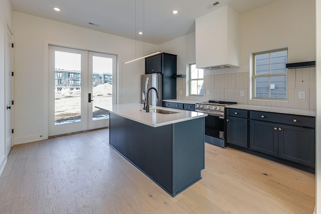 kitchen with an island with sink, stainless steel appliances, light countertops, french doors, and premium range hood