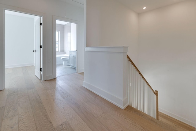 hallway with light wood-type flooring, recessed lighting, baseboards, and an upstairs landing