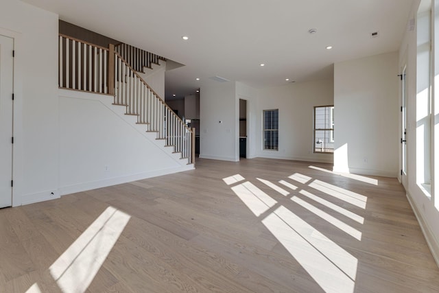 unfurnished living room with stairs, light wood-style flooring, and a healthy amount of sunlight