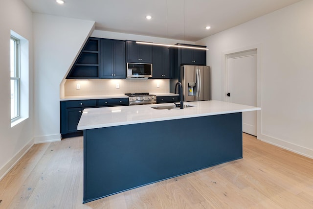 kitchen with decorative light fixtures, stainless steel appliances, light countertops, a kitchen island with sink, and a sink