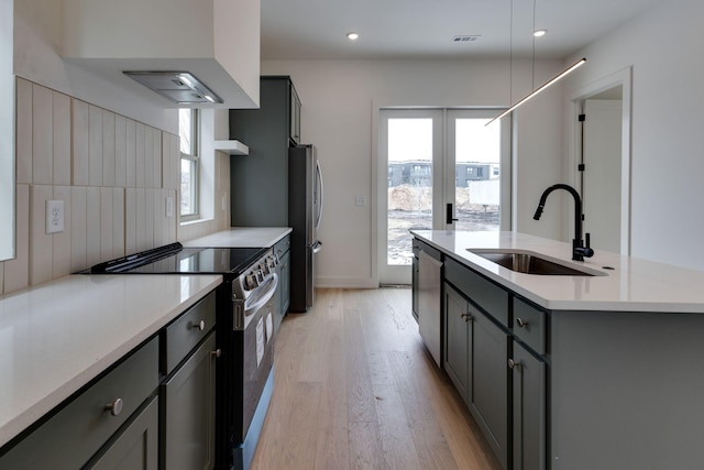 kitchen featuring appliances with stainless steel finishes, light countertops, a sink, and a center island with sink