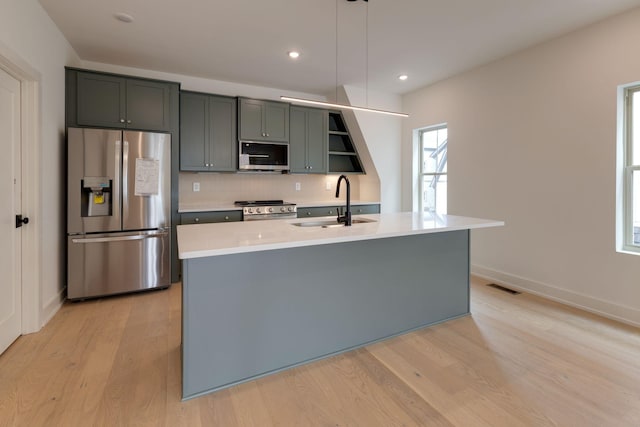 kitchen with stainless steel appliances, light countertops, decorative light fixtures, and a kitchen island with sink