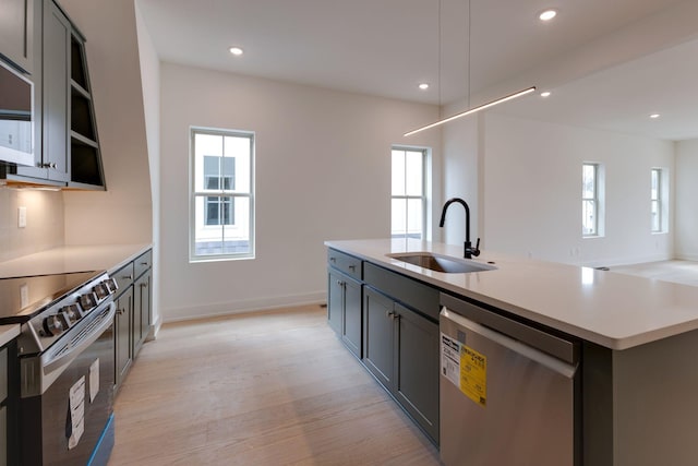 kitchen featuring a kitchen island with sink, appliances with stainless steel finishes, light countertops, and a sink