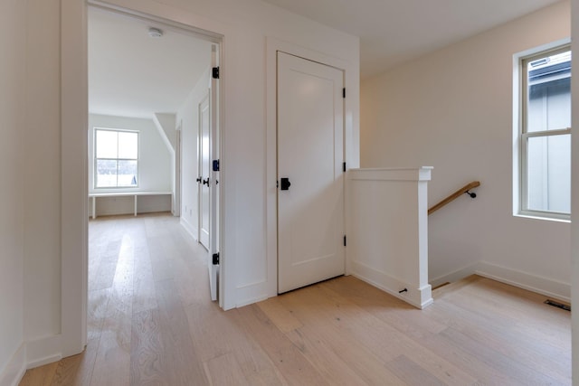 hall with visible vents, light wood finished floors, an upstairs landing, and baseboards