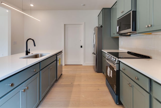 kitchen featuring light wood-style flooring, a sink, light countertops, appliances with stainless steel finishes, and backsplash