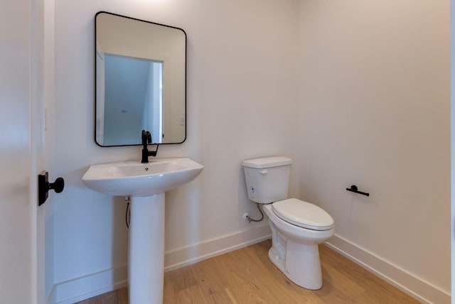 half bath with toilet, baseboards, and wood finished floors