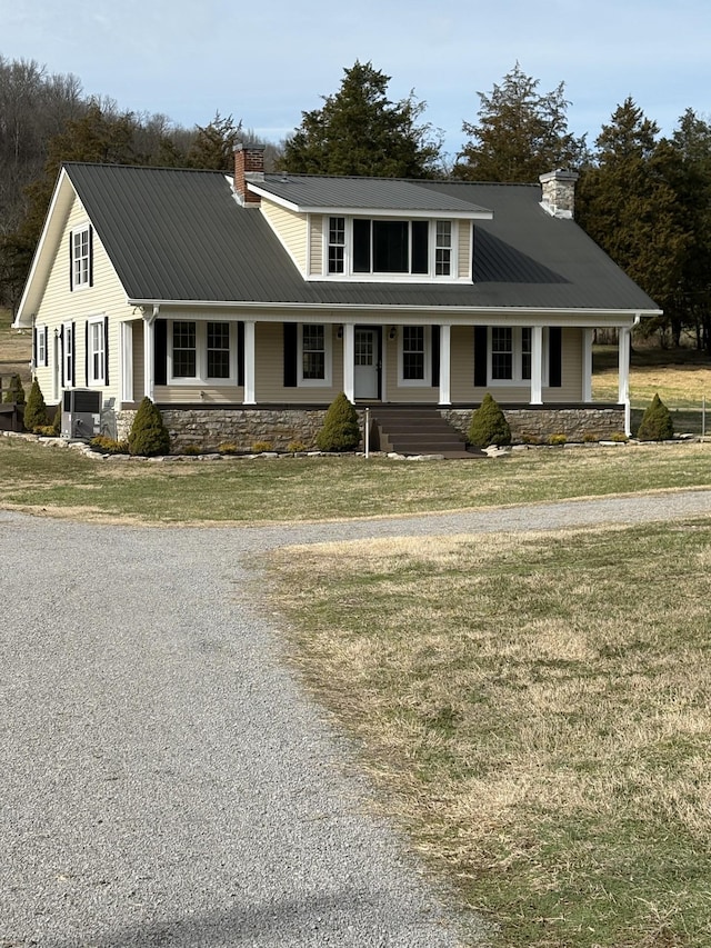 view of front of house with stone siding, a chimney, metal roof, covered porch, and a front yard