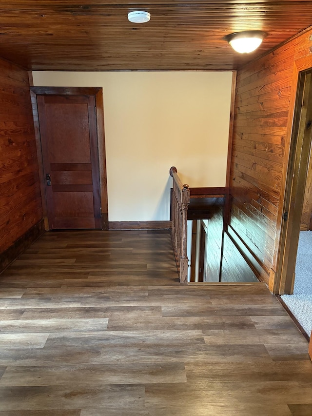 hall with dark wood-type flooring, wooden ceiling, wooden walls, and an upstairs landing