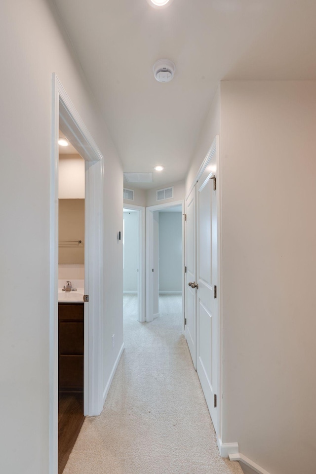 hall featuring baseboards, visible vents, and light colored carpet