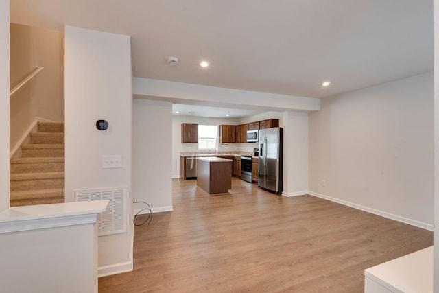 kitchen with stainless steel appliances, a kitchen island, visible vents, open floor plan, and brown cabinets