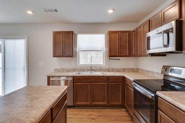 kitchen featuring stainless steel appliances, a sink, visible vents, light countertops, and brown cabinets