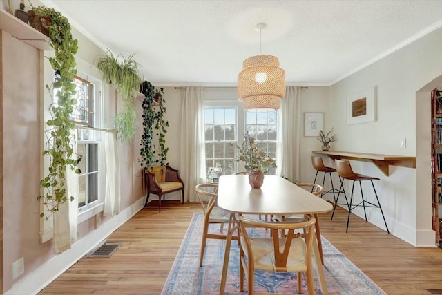 dining space with baseboards, ornamental molding, visible vents, and light wood-style floors